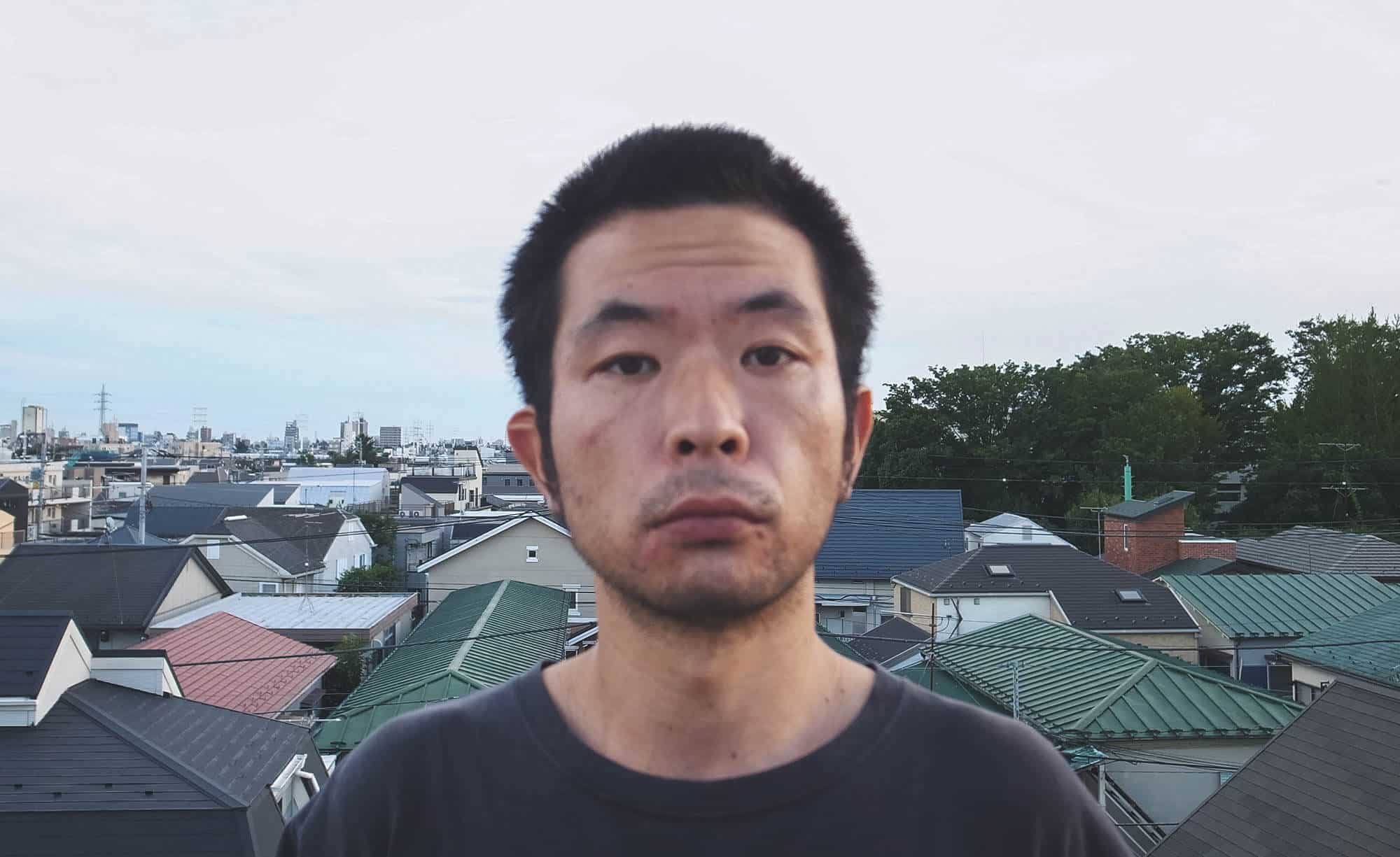 DirAct workshop ディラクト ワークショップ - 都市部の屋根群を背に立つ男性の横顔と空、演技の練習を連想させる表情、スクール風の雰囲気を感じる風景