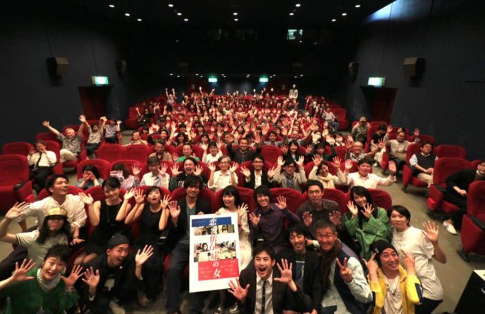 DirAct workshop ディラクト ワークショップ - 大規模な会場で手を挙げ笑顔の集合写真、スクールでの演技を学ぶ映画好きの仲間たちが前方のポスターを掲げる